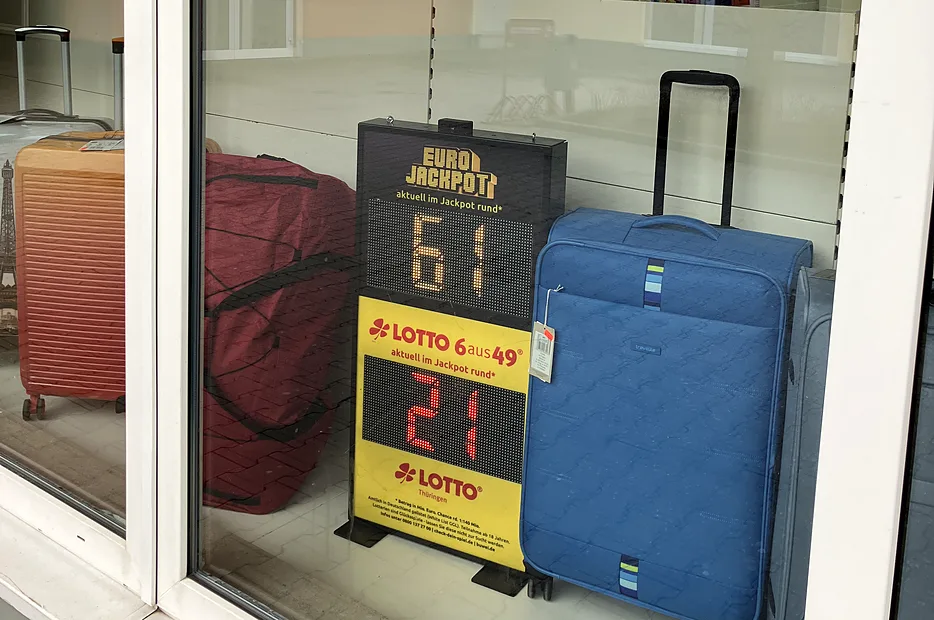 Digitales LOTTO Jackpot-Display in einem Schaufenster neben Reisegepäck